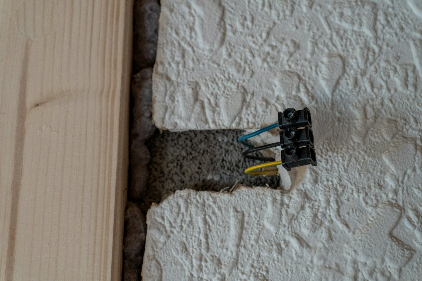 Electrician installing blue and yellow wires in a wall.
